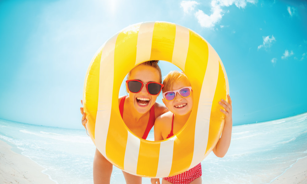 Mom and Daughter smiling through a yellow and white striped tube on a beach