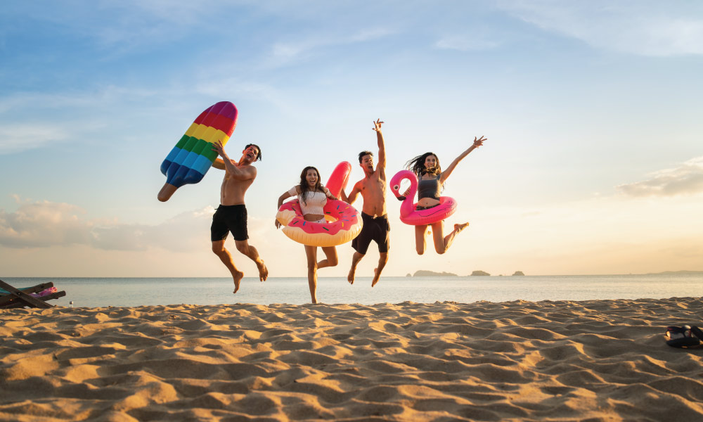 Adult friends jumping on the beach with inflatable pool toys