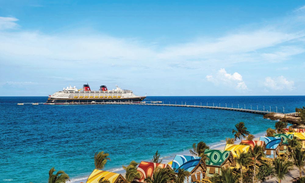 Disney Cruise Ship docked at privat island with colorful umbrellas on the beach with chairs