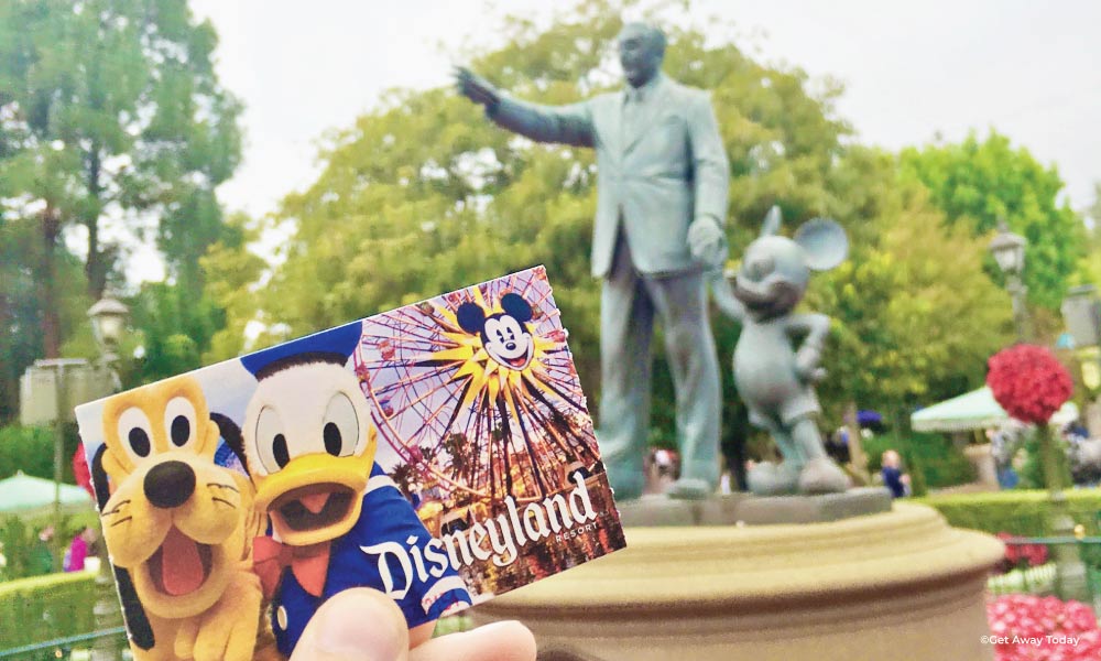 Disneyland ticket with Donald and Pluto held up in front of Walt and Mickey Statue