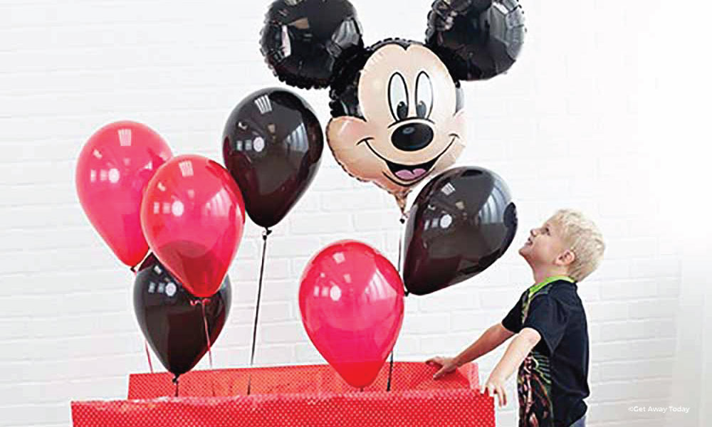 Boy opening a large red present with red, black and a large mickey balloon coming out