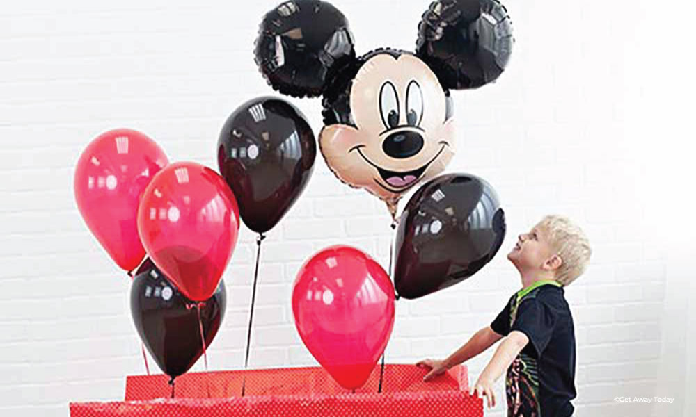 Young boy opening a large red present with a Mickey balloon coming out