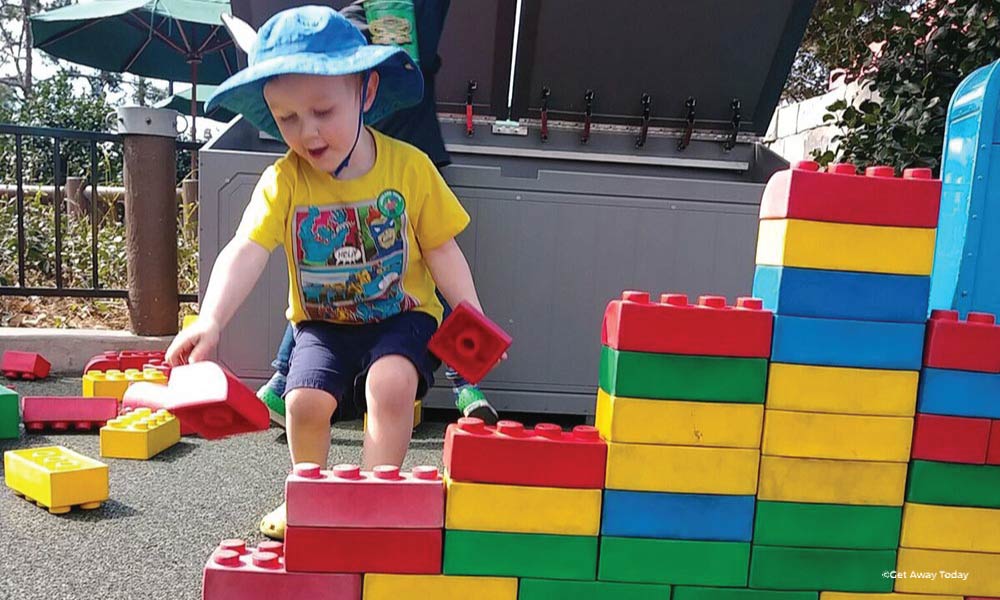 Toddler in a sun hat playing with giant lego blocks