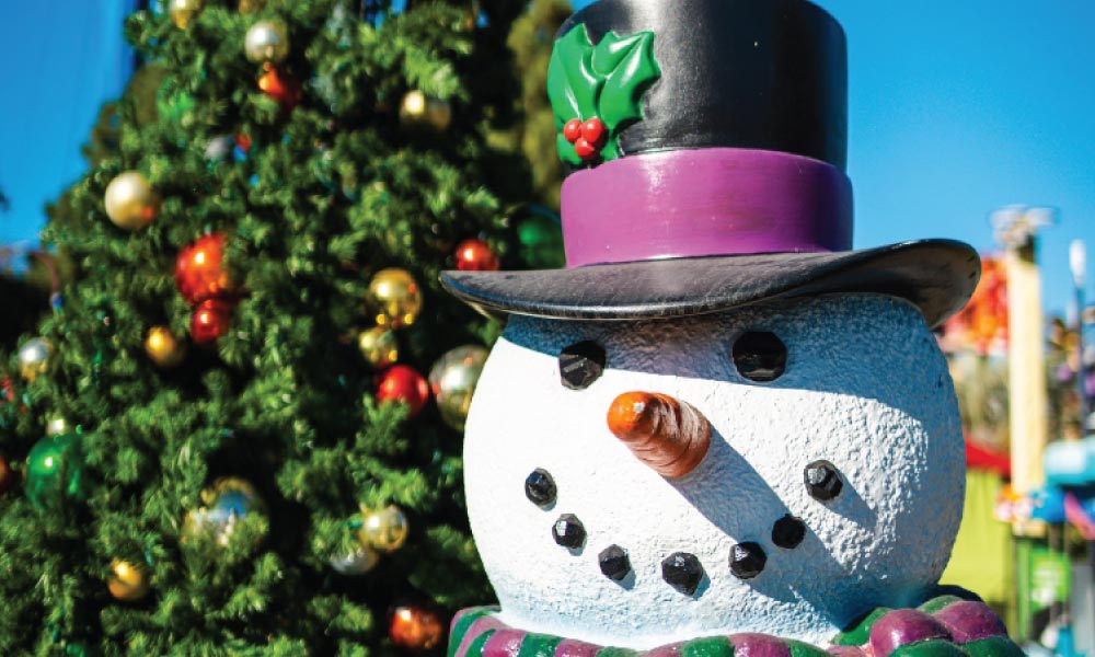 Snowman statue with tophat in front of a christmas tree