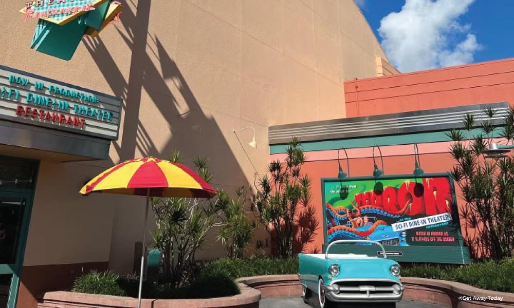 Exterior of Sci Fi Diner with a light blue old car and a red and yellow umbrella