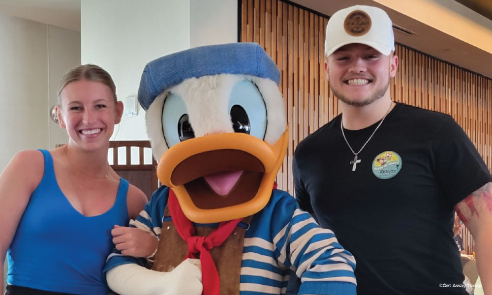 Two young adults posing with Donald Duck in a Sailor's outfit