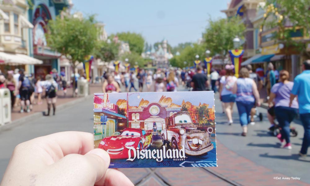 Disneyland ticket with Mater and Lightning McQueen being held up on Main Street USA