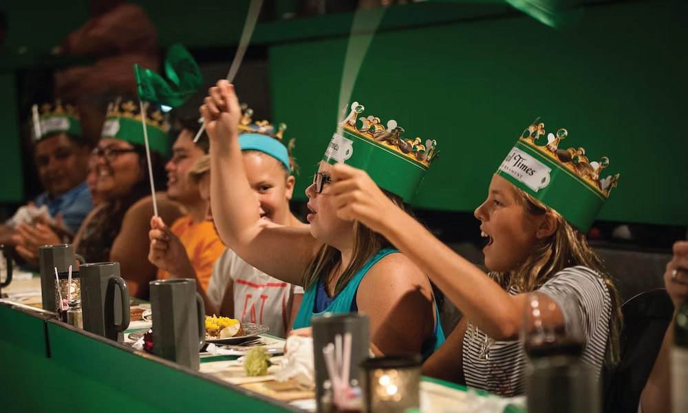 Kids with green paper crowns waving flags and eating their lunch