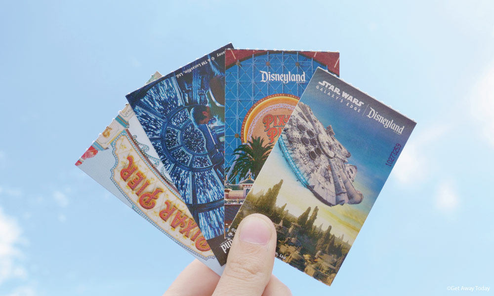 Four Disneyland tickets being held up to the sky