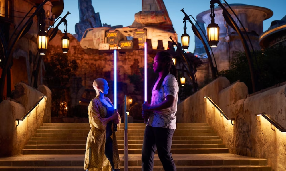 Man and woman posing as Jedis at night in Star Wars Galaxy's Edge in Disneyland