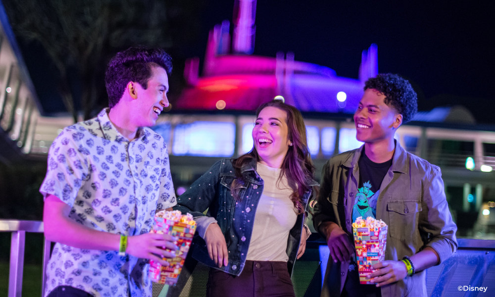 Friends leaning against a railing eating Disney popcorn and laughing