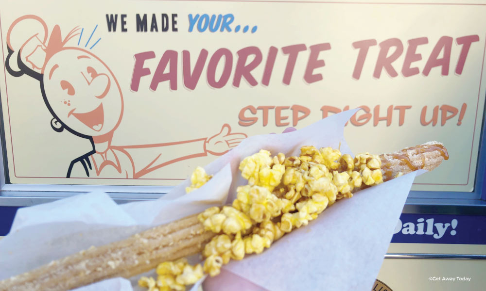 Churro with popcorn on top near a churro cart in Disneyland