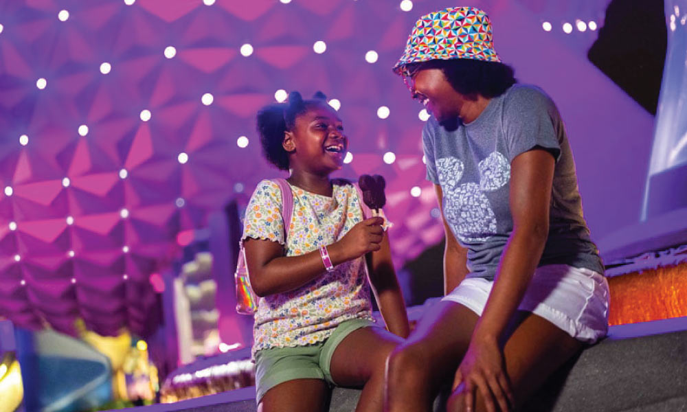 Sisters sitting near the EPCOT Ball eating Mickey Ice Cream Bars together