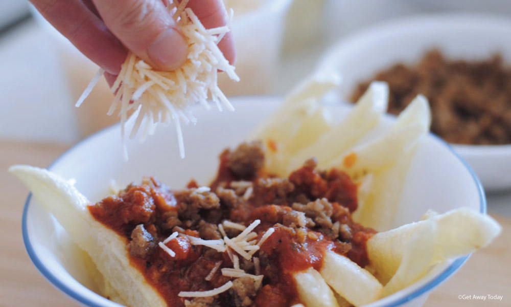 parmesan cheese being sprinkled on italilan poutine in a bowl