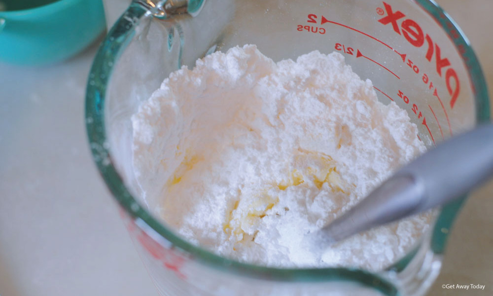 frosting ingredients getting mixed in a glass liquid measuring cup