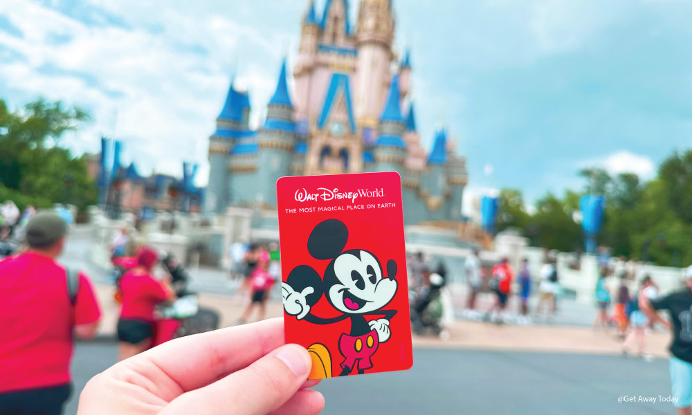 Red Disney World Ticket and Key Card held up in front the Cinderella Castle