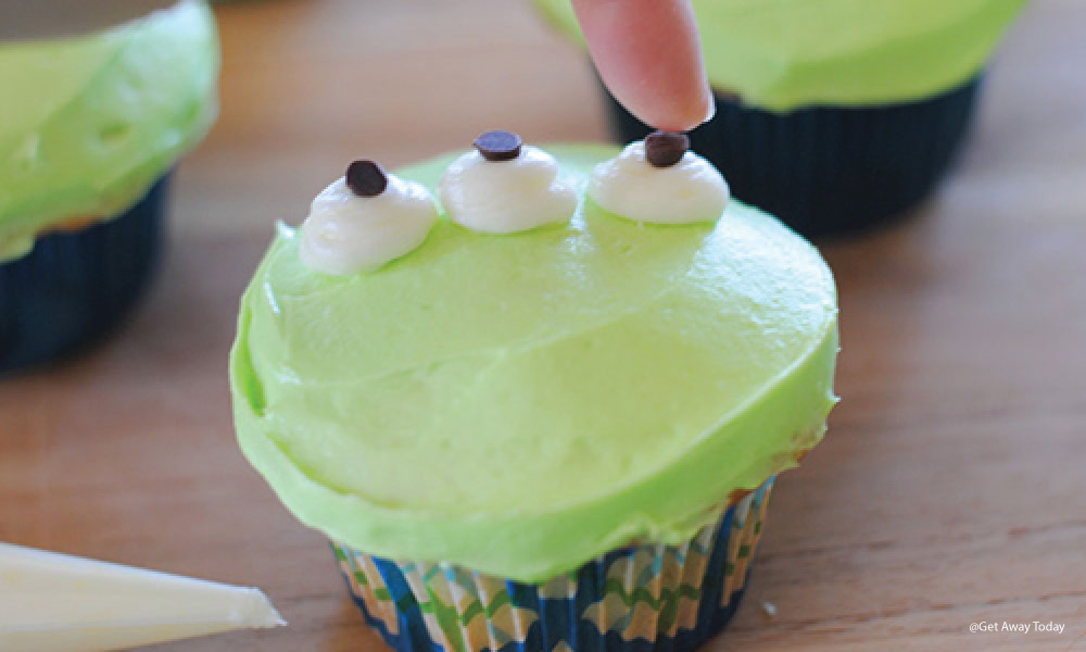 green frosted cupcake with three frosting eyes and tiny chocolate chips added as pupils